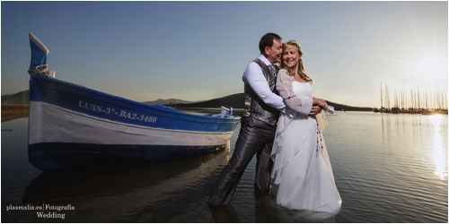 Junto a una barca varada en la playa una pareja de novios se abraza en su reportaje de fotografía post-boda