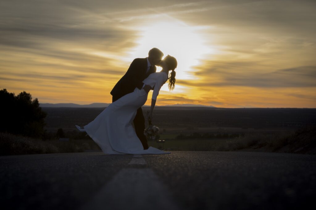 Fotos de boda al atardecer: los novios se besan a contraluz en una carretera al ponerse el sol